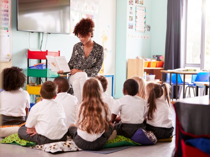 Young teach reading to a group of primary school students in classroom